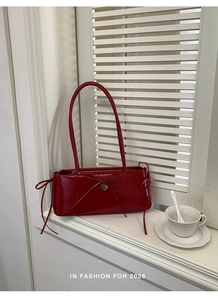 Detail of red glossy leather shoulder bag with bow and heart pendant on window sill