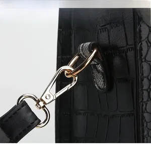 Macro detail of glossy golden metal lobster clasp on black crocodile textured leather bag