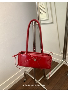 Close-up of a red patent leather underarm bag with a bow and heart-shaped metal charm