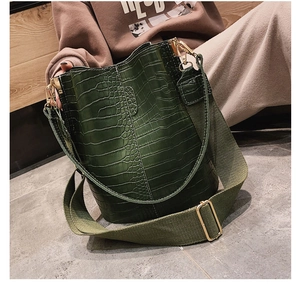 Detail of dark green crocodile texture bucket bag with wide canvas strap and gold hardware