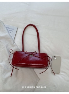 Detail of red leather shoulder bag with decorative bow and heart-shaped metal pendant