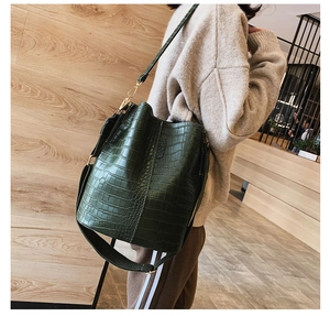 Detail of dark green crocodile pattern bucket bag with wide and thin straps