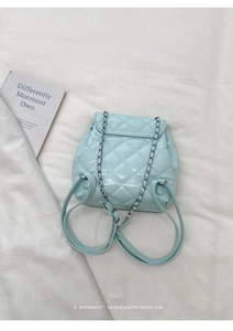 Close-up of mint green quilted leather backpack with silver chain strap on beige fabric