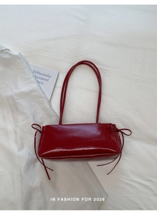 Detail of dark red high-gloss shoulder bag featuring decorative side ribbons on white linen