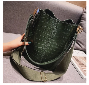 Detail of dark green crocodile pattern bucket bag with wide fabric shoulder strap