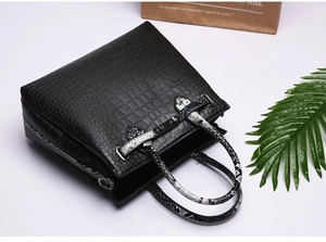 Detail of black embossed faux crocodile leather handbag with snake print handles