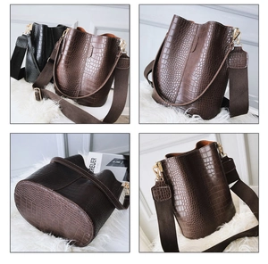 Detail of crocodile embossed bucket bag featuring wide canvas strap and gold hardware