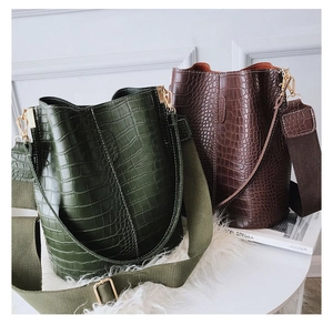 Detail of crocodile pattern bucket bag with wide strap and golden hardware