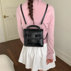 Elegante mochila de cuero negro con lazos mostrada en una modelo con un estilo de campus