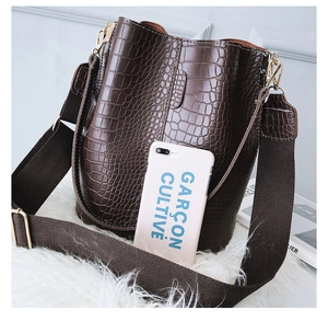Detail of dark brown crocodile pattern bucket bag with wide canvas strap and gold hardware