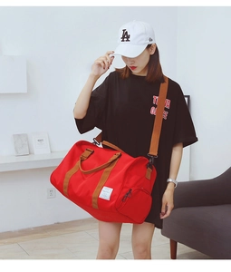 Détail du grand sac de voyage rouge avec sangles brunes et poche latérale zippée