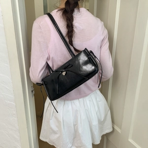 Glossy black shoulder bag with bow and heart charm shown on model back view