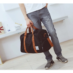 Détail du sac de sport noir avec poignées brunes et écusson décoratif blanc