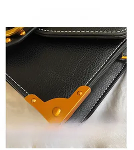 Detailed view of black litchi pattern leather bag with white stitching and gold metal corners