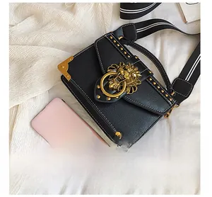 Detail of black leather crossbody bag with golden lion head buckle and rivet studs