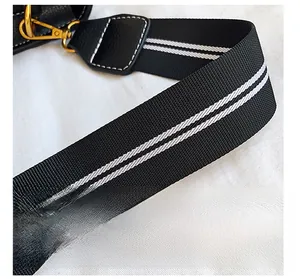 Detail of striped woven shoulder strap with black leather and gold metal hooks