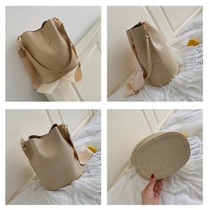 Detailansicht der beigen Bucket Bag mit Krokodilprägung, breitem Gurt und goldener Hardware