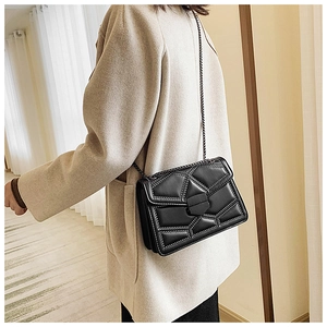 Side view of a black studded crossbody chain bag worn with a beige wool coat
