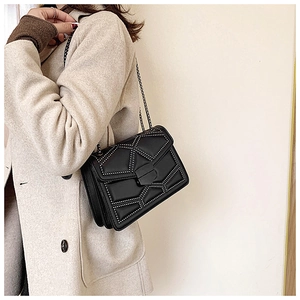 Detail of black rivet crossbody bag on model with beige coat and silver chain strap