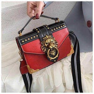 Detail of lion head clasp and gold studs on red and black leather handbag