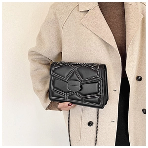 Detail of black quilted crossbody bag with silver studs on elegant beige coat
