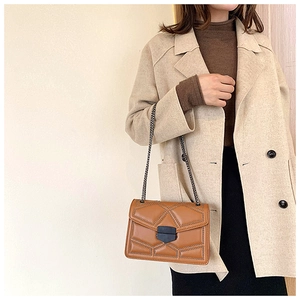 Detail of brown quilted shoulder bag with metal studs and chain strap on a model