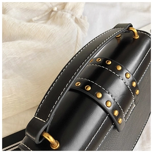 Close-up of black leather bag featuring golden studs and white contrast stitching detail
