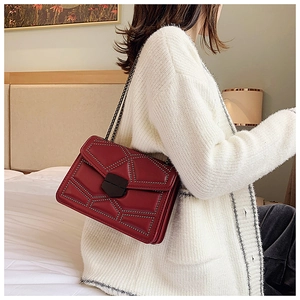 Close-up of burgundy quilted chain bag with rivet details worn over a white sweater