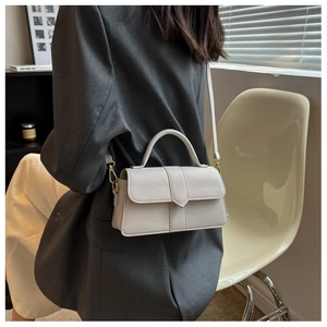 Detail of a creamy white small crossbody bag with gold hardware worn with a grey blazer