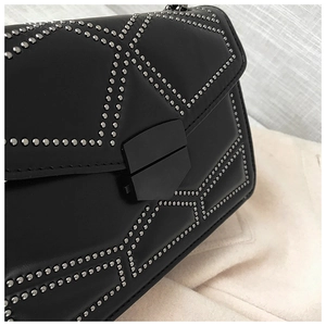 Detail of black leather crossbody bag with silver studs and matte black metal buckle