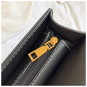Macro view of gold-tone metal zipper and smooth black leather texture on hand bag