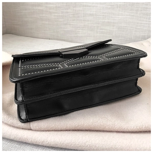 Detail view of the black leather bag with metal rivets and multi-layer gusset design
