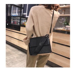 Sac bandoulière noir motif crocodile porté par un mannequin dans un café