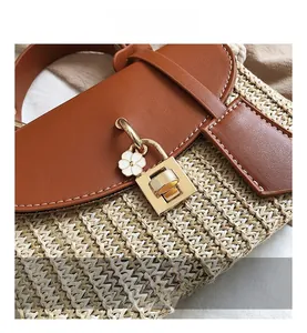 Close-up of woven straw bag with brown leather flap and golden metal twist lock
