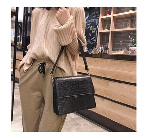 Détail du sac noir à motif crocodile avec boucle dorée et large bandoulière