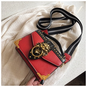 Detail of red pebbled leather crossbody bag with gold lion head and rivet accents
