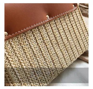 Close-up of straw woven bag featuring a brown leather flap and golden rivet details