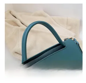 Macro view of blue-green leather tote handle with golden hardware and precise stitching