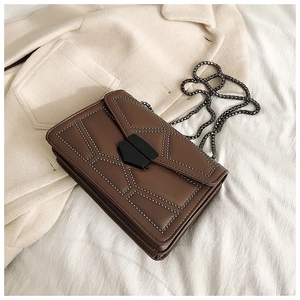 Detail of dark brown leather crossbody bag with rivet accents and metal chain on a coat