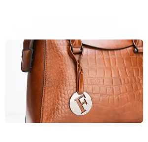 Macro shot of brown crocodile pattern handbag detail with a silver letter F metal charm