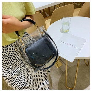 Transparent PVC tote with gold metal handle and black inner pouch on a white table