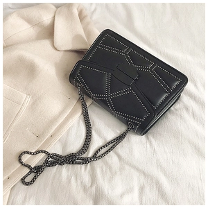 Detail of black crossbody bag with silver rivets and metal chain on beige coat background