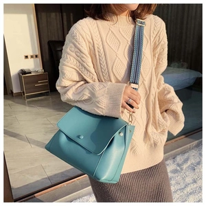 Detail of light blue crossbody bag featuring a wide decorative woven shoulder strap