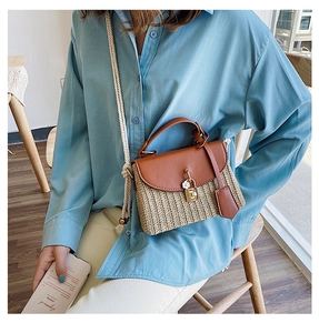 Close-up of woven straw bag with brown leather flap, gold lock and flower charm