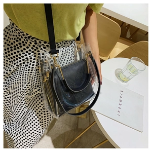 Detail of transparent PVC bucket bag with black inner pouch and gold-tone hardware on a table