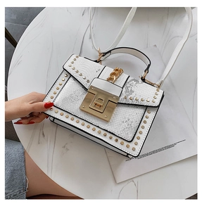 Detailed view of a white snake-textured handbag with gold rivets and square buckle on marble