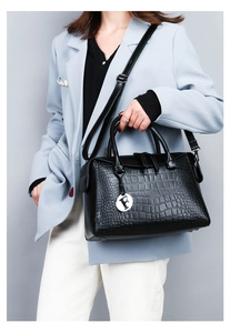 Detail of black crocodile-embossed tote bag featuring a silver F-letter pendant and texture