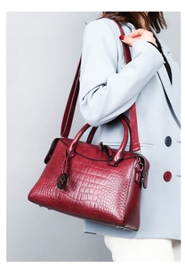 Detail view of red crocodile embossed leather handbag with metal H charm and texture