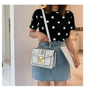 Detailed close-up of white embossed leather crossbody bag with gold studs and chain strap