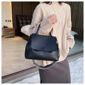 Close-up of black leather handbag with a patterned woven shoulder strap and round buckle